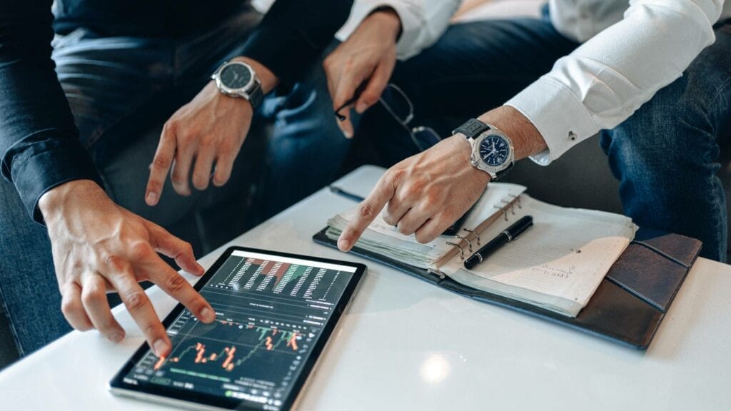 two people pointing at a tablet on a white table analyzing cryptocurrencies stock.